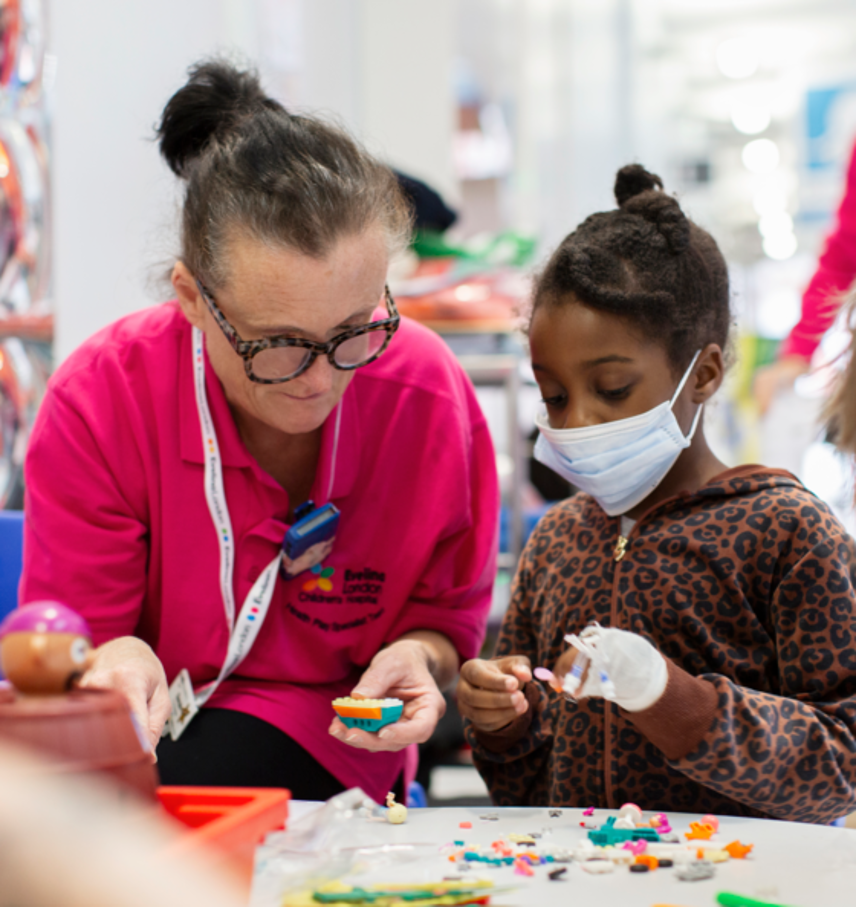 child with face mask and bandaged hand playing lego with health play specialist